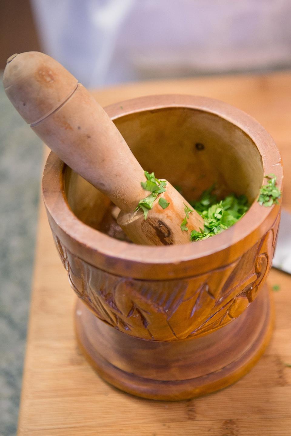 Garlic, herbs and other ingredients for sofrito seasoning are placed in my carved-wood pilón (mortar and pestle) for pounding into a paste.