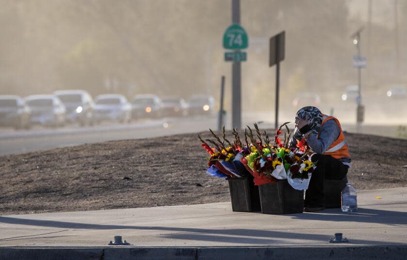 SAN JACINTO, CA - NOVEMBER 24, 2022: Juan Star covers his face as powerful wind gusts blows sand and dirt across the intersection where he is selling flowers on Thanksgiving day on November 24, 2022 in San Jacinto, California. The power is out in the area of Highway 74 and Vista Place. The San Ana winds will continue through Friday.(Gina Ferazzi / Los Angeles Times)