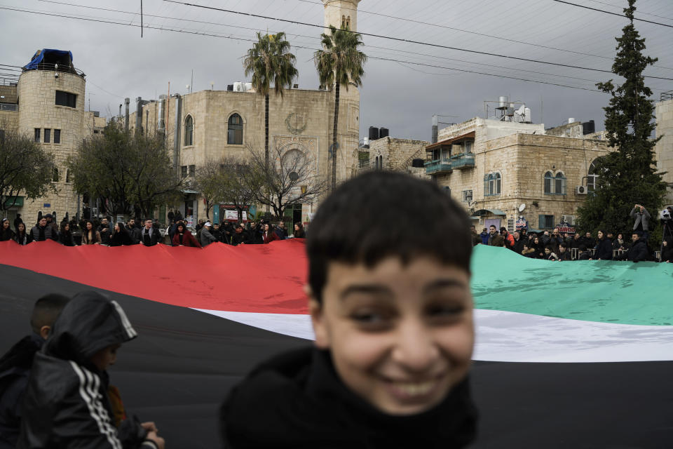 People hold a giant Palestinian flag in Manger Square, near the Church of the Nativity, traditionally believed to be the birthplace of Jesus, on Christmas Eve, in the West Bank city of Bethlehem, Sunday, Dec. 24, 2023. Bethlehem is having a subdued Christmas after officials in Jesus' traditional birthplace decided to forgo celebrations due to the Israel-Hamas war. (AP Photo/Leo Correa)