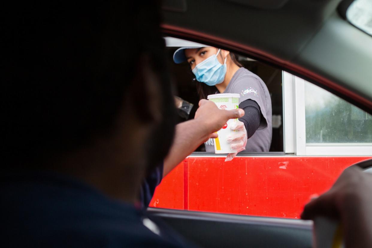 Prince Rupert, Canada - May 17, 2020. A man reaches for his food at the McDonalds drive-thru window as the employee wears a mask for protection.