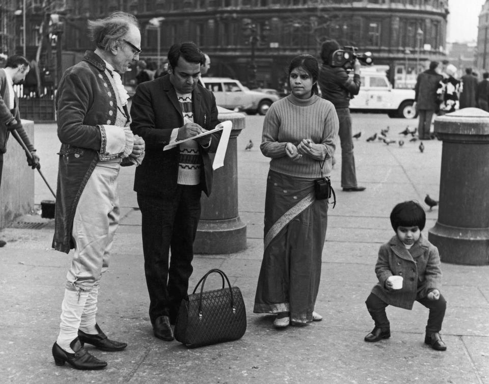 A man in eighteenth century dress asks an Indian couple to sign a petition against the government's attempt to save energy with a three-day working week, Leicester Square, London, 21st February 1974. The petition is to be presented to British Prime Minister Edward Heath.  (Photo by P. Wade/Fox Photos/Hulton Archive/Getty Images)