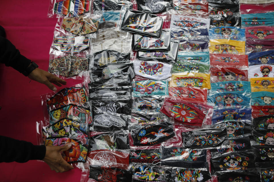 Luis Fuentes, 45, from Ecuador, gathers up face masks decorated with traditional Mexican designs, as he puts away his wares as it begins to rain, on Insurgentes Avenue in Mexico City, Monday, Aug. 17, 2020. Fuentes, who has been in Mexico for eight years, used to sell Mexican handicrafts at special events inside shopping malls, but since the beginning of the coronavirus pandemic, he has been forced to sell informally on the street. (AP Photo/Rebecca Blackwell)