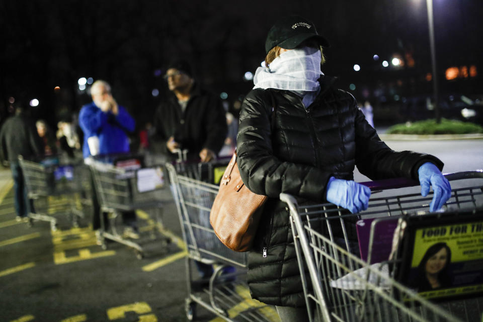 FILE- In this March 20, 2020 file photo customers wearing protective masks and gloves wait in line at a Stop & Shop supermarket in Teaneck, N.J., that opened special morning hours to serve people 60-years and older due to coronavirus concerns. The virus's rampage through the New York metro region, from the well-to-do towns along Connecticut's coastline to the bedroom communities of northern New Jersey and Long Island, offers a counterweight to the notion of the suburbs, with their plentiful open spaces, as havens safe against the coronavirus. (AP Photo/John Minchillo, File)