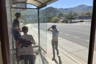 Teenage boys wait for a public bus after a pickup game of soccer in Los Alamos, N.M., on Thursday, May 12, 2022, during a weeklong public school closure because of nearby wildfire. The blaze has been creeping closer to the mesa-top city and companion Los Alamos National Laboratory that analyzes global threats of disease, warfare and natural disasters. Scientists at Los Alamos are using supercomputers and ingenuity to improve wildfire forecasting and forest management amid drought and climate change in the American West. (AP Photo/Morgan Lee)