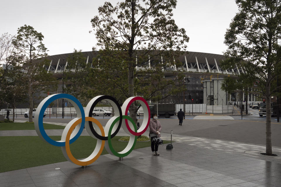 A woman pauses for photos next to the Olympic rings near the New National Stadium in Tokyo, Monday, March 23, 2020. The IOC will take up to four weeks to consider postponing the Tokyo Olympics amid mounting criticism of its handling of the coronavirus crisis that now includes a call for delay from the leader of track and field, the biggest sport at the games. (AP Photo/Jae C. Hong)