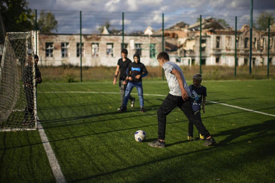 Boys play soccer next to a destroyed school, background, in Izium, Ukraine, Monday, Oct. 3, 2022. (AP Photo/Francisco Seco)