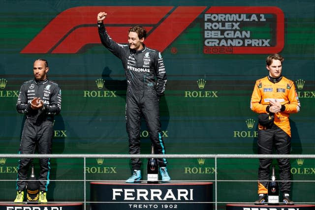 Russell raises his hand in celebration on the podium alongside Hamilton (left) and Oscar Piastri (right)