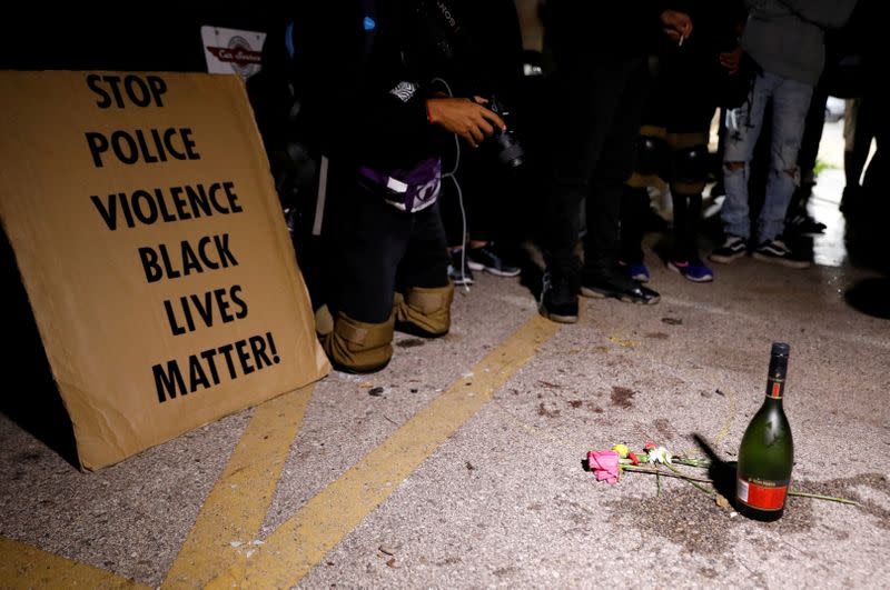 Imagen de n cartel que pide parar la violencia policial cerca de una botella de alcohol y flores colocadas en tributo a las víctimas de las personas baleadas en las manifestaciones del martes en la noche tras los disparos de un policía a Jacob Blake, un hombre negro, en Kenosha, Wisconsin, EEUU