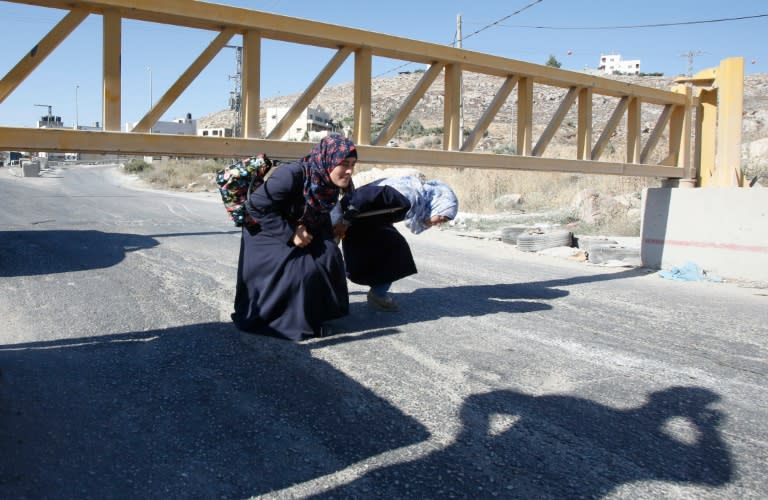Palestinian women pass under a barrier blocking the road at the southern entrance to the West Bank city of Hebron, on July 2, 2016
