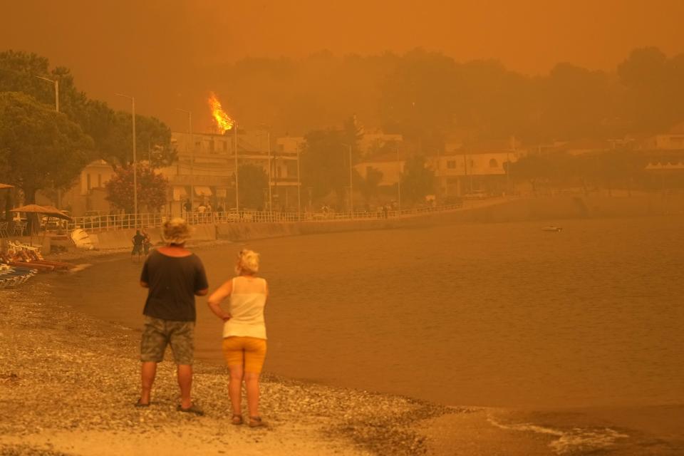 Fire burns trees near a beach at Pefki village on Evia island, about 189 kilometers (118 miles) north of Athens, Greece, Sunday, Aug. 8, 2021. Pillars of billowing smoke and ash are blocking out the sun above Greece's second-largest island as a days-old wildfire devours pristine forests and triggers more evacuation alerts. (AP Photo/Petros Karadjias)