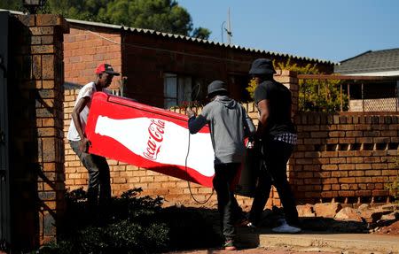 Locals carry a Cocacola branded refrigerator they looted at a nearby shop during protests in Atteridgeville, a township located to the west of Pretoria, South Africa June 21, 2016. REUTERS/Siphiwe Sibeko