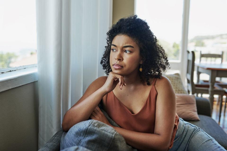 shot of a young woman looking pensively out a window at home