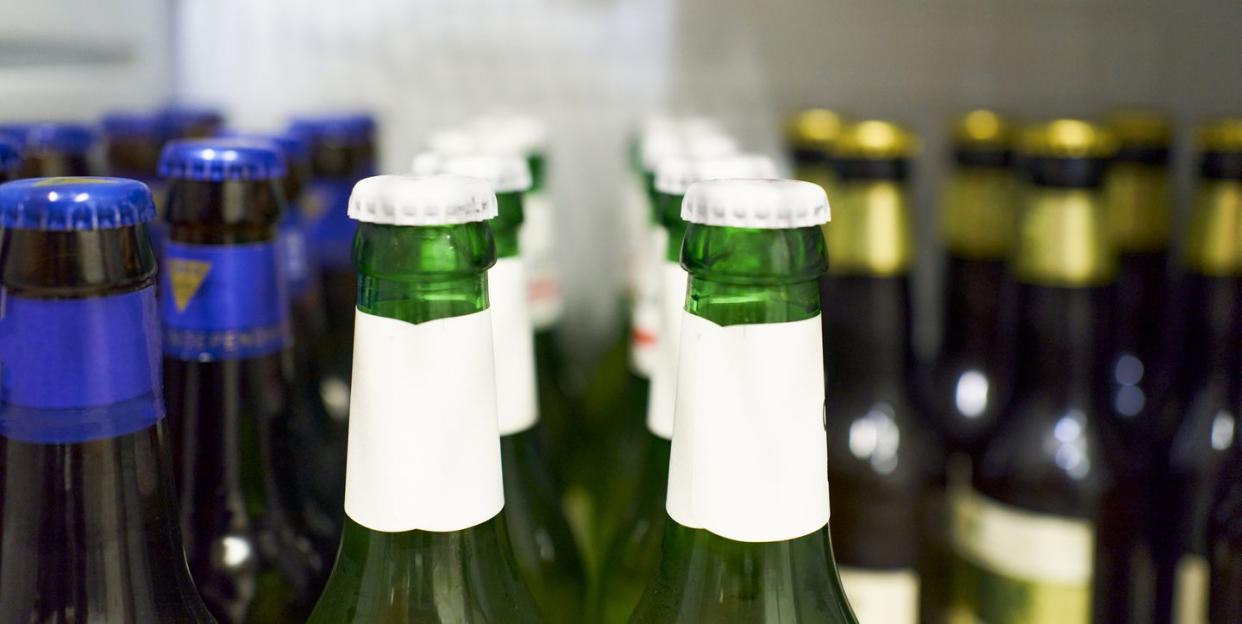 close up of beer bottles with white cap and beers with blue and gold details in the background inside the refrigerator