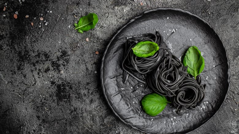 black squid ink pasta on a black plate with green basil