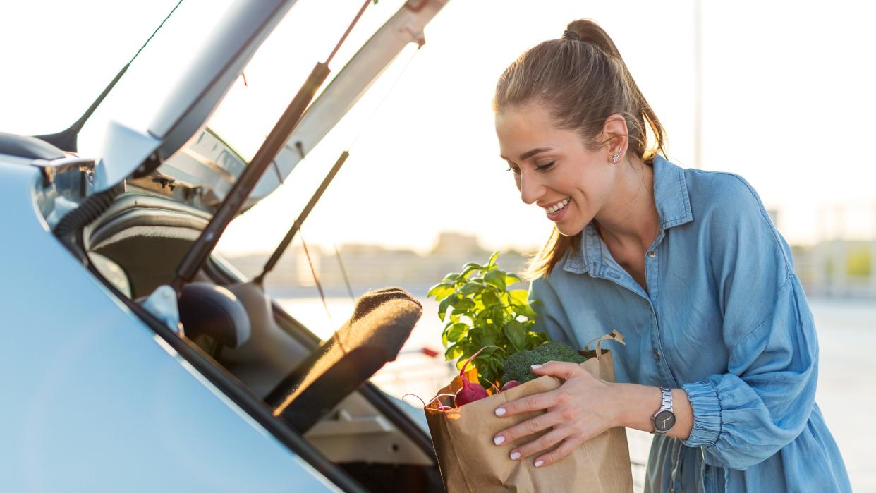 Young woman in car park carrying shopping bag of groceries.