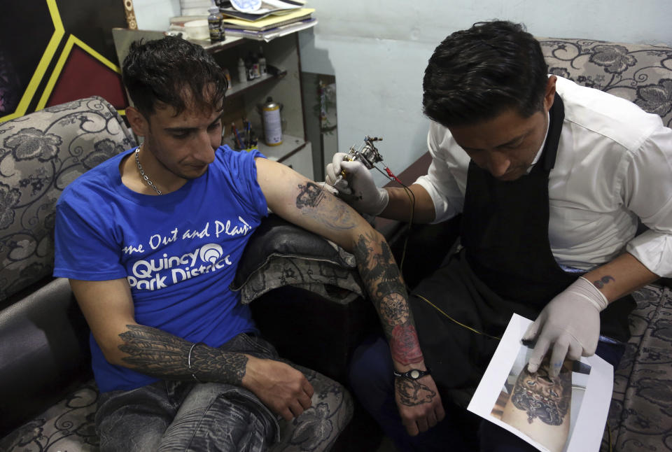 In this Wednesday, Nov. 20, 2019, photo, Omid Noori, 23, left, gets a lion tattoo on his left arm by Nazeer Mosawi, a tattoo artist in Kabul, Afghanistan, Mosawi, 42, fought for seven years in Afghanistan’s civil war with the Islamic insurgents. He says he is still fighting the war, but this time his battle is against society’s conservatism, with his tattoo machine as his weapon. (AP Photo/Rahmat Gul)