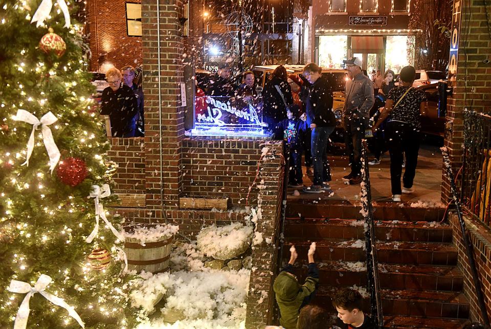 Children and adults gather in artificial snow in front of American Shoe at 816 E. Broadway during last year's Living Windows.