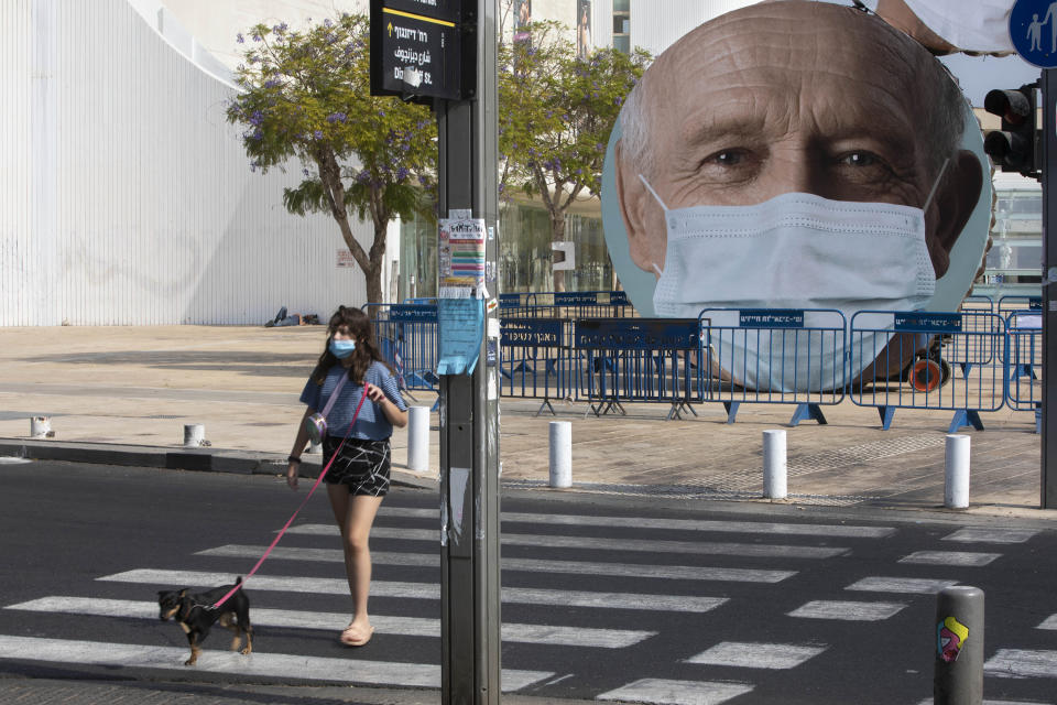 An Israeli woman walks past banners encouraging people to wear face masks in Tel Aviv, Israel, Thursday, Sept. 24, 2020. Israeli Prime Minister Benjamin Netanyahu on Wednesday announced plans for a strict, two-week nationwide lockdown in a bid to slow a raging coronavirus outbreak. (AP Photo/Sebastian Scheiner)