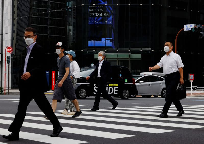 People pass by an electronic screen showing Japan's Nikkei share price index inside a commercial building in Tokyo