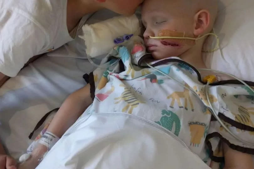 George Woodall asleep being kissed by his brother Alex Woodall holding hands post cancer resection surgery.