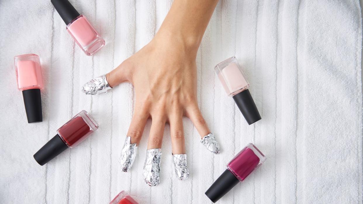 female hand with strips of foil on fingers and nail polishes on towel