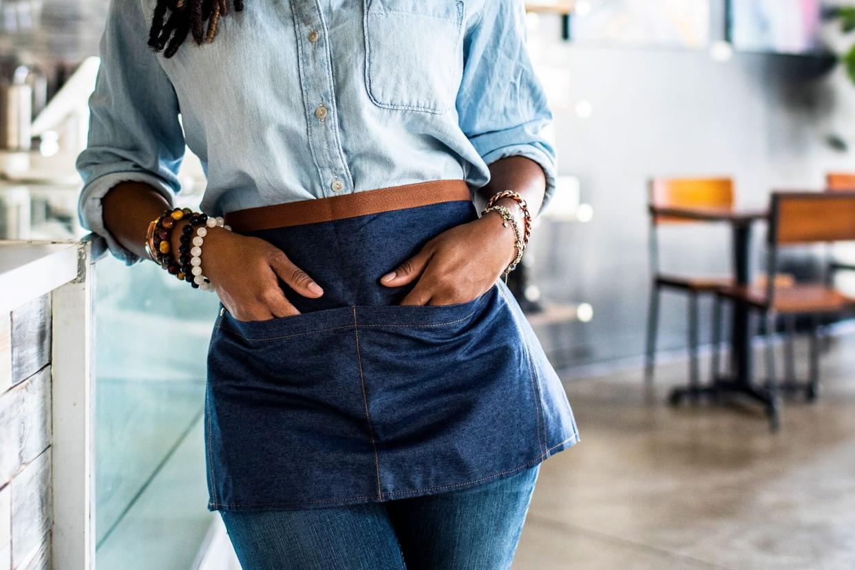 A restaurant server with their hands in their pockets