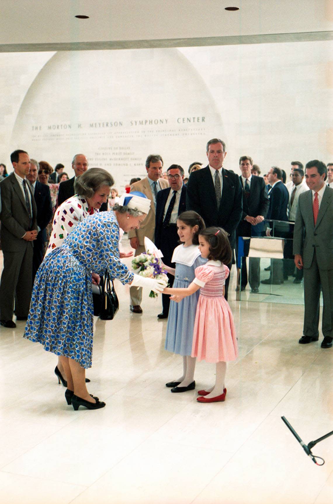 Queen Elizabeth II accepts flowers and a gift from two young girls at the Morton H. Meyerson Symphony Center in Dallas on May 21, 1991. Dallas Mayor Annette Strauss seen on her left.