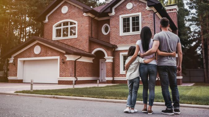 Back view of happy family is standing near their modern house and hugging.