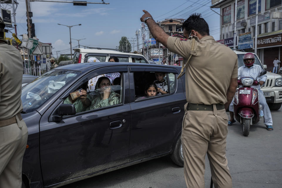 A Kashmiri family seeks permission from a police officer to cross a road near a checkpoint during restrictions in Srinagar, Indian controlled Kashmir, Sunday, Aug. 7, 2022. Authorities had imposed restrictions in parts of Srinagar, the region's main city, to prevent gatherings marking Muharram from developing into anti-India protests. (AP Photo/Mukhtar Khan)