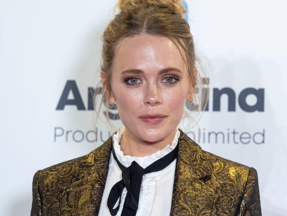 Actress Katia Winter wearing a gold blazer, white shirt, and black tie at a red carpet in France in October 2019.