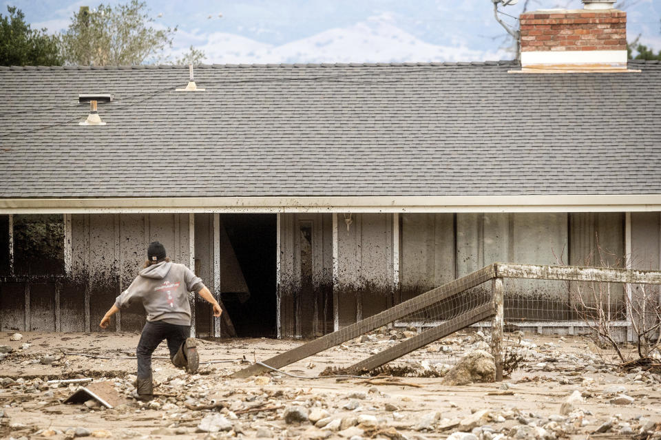 A man crosses mud while recovering belongings from a neighbor's home which was damaged in a mudslide on Wednesday, Jan. 27, 2021, in Salinas, Calif. The area, located beneath the River Fire burn scar, is susceptible to mudslides following last year's wildfires. (AP Photo/Noah Berger)