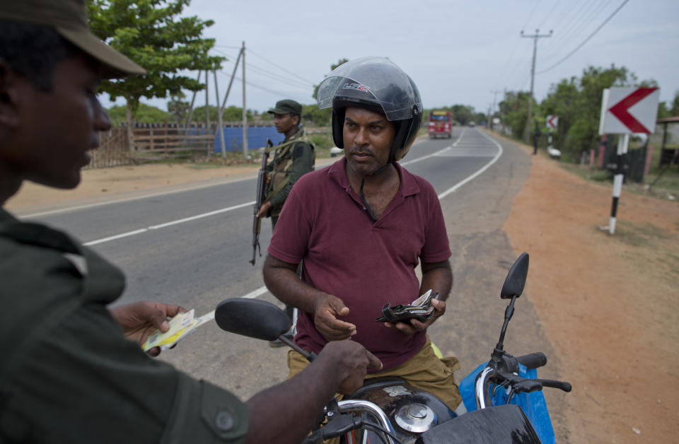 An army officer checks the identity of a man on a motor bike at a roadside checkpoint in Kalmunai, Sri Lanka, Sunday, April 28, 2019. Police in Ampara showed The Associated Press on Sunday the explosives, chemicals and Islamic State flag they recovered from the site of one security force raid in the region as Sri Lanka's Catholics celebrated at televised Mass in the safety of their homes. (AP Photo/Gemunu Amarasinghe)