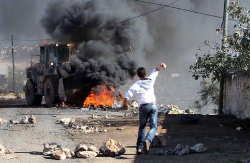 A Palestinian protester throws a stone at an Israeli bulldozer during a demonstration against the expropriation by Israel of the West Bank village of Kafr Qaddum, near Nablus, on November 30, 2012. Israel is to build 3000 new settler homes in east Jerusalem and the West Bank after the Palestinians won recognition as a non-member state at the United Nations