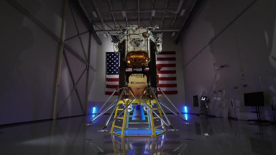 Intuitive Machines' Odysseus Nova-C lander is pictured in front of an American flag in a dimly lit storage room.