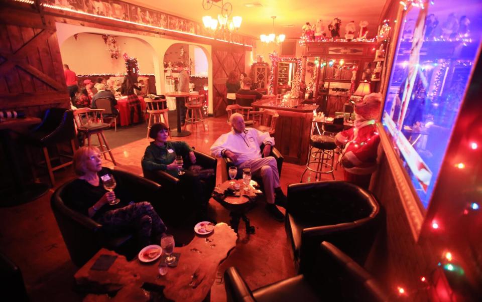 Several people gather in chairs near at large-screen television in a warmly lit bar