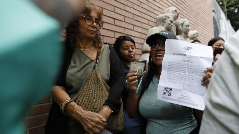 Mujer muestra su identificacion con una carta en fila de votación 
