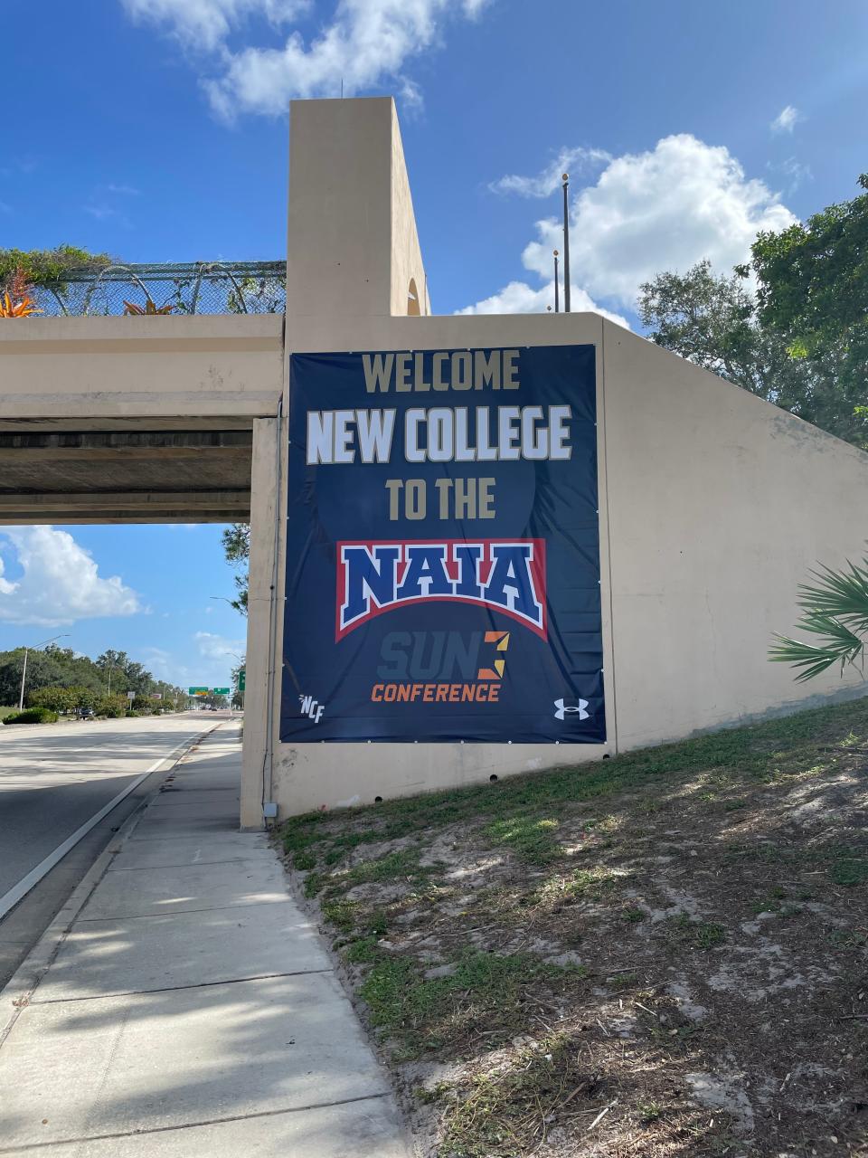 A sign draped on the side of a bridge near New College of Florida's campus on Tamiami Trail announces the college's acceptance into the National Association of Intercollegiate Athletics on Monday, Oct. 2, 2023.