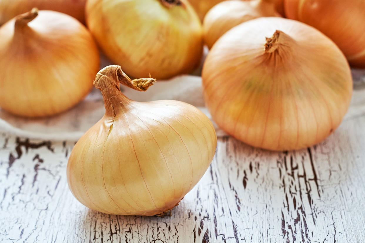 Closeup of a yellow onion with several surrounding it and in the background on a rustic white wooden table