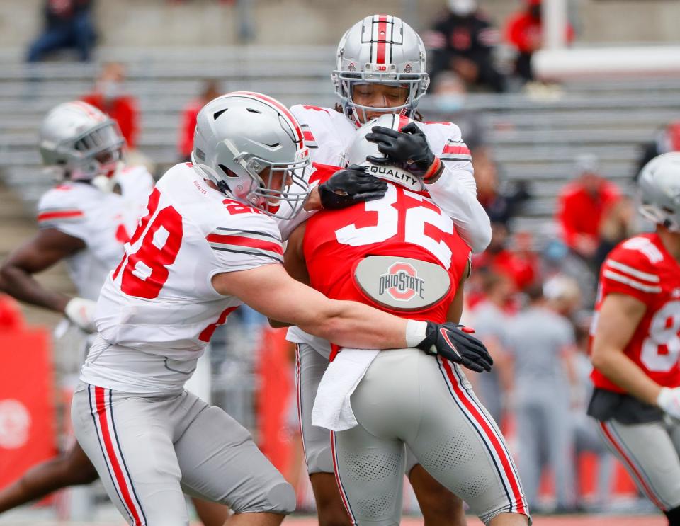 Team Brutus safety Ronnie Hickman (14) and linebacker Reid Carrico (28) tackle Team Buckeye running back TreVeyon Henderson (32) during the Ohio State Buckeyes football spring game at Ohio Stadium in Columbus on Saturday, April 17, 2021. 