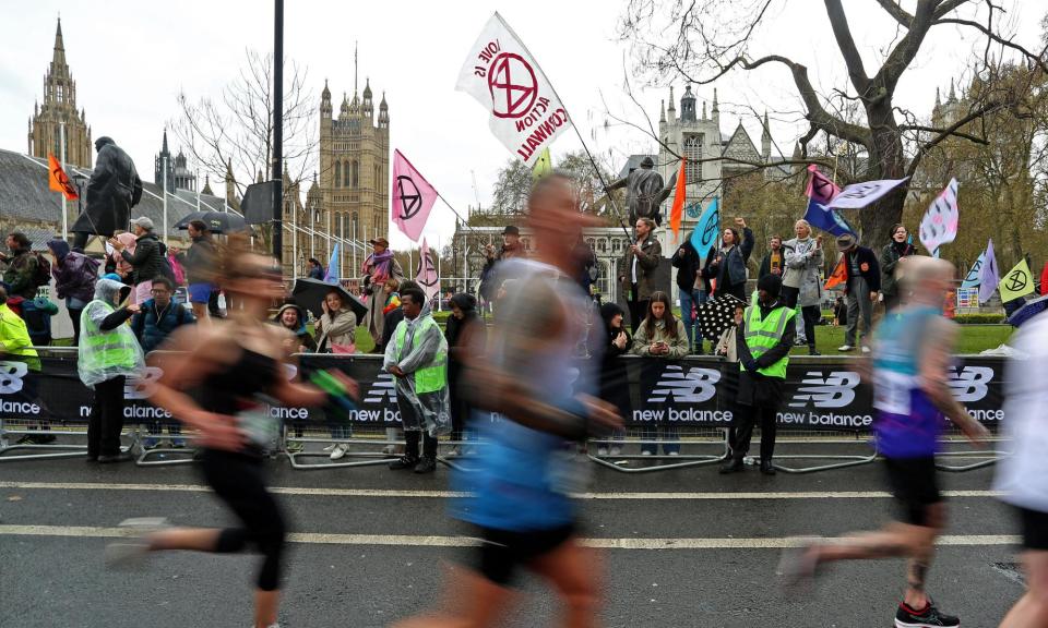 <span>Extinction Rebellion members wave flags while spectating the 2023 London Marathon.</span><span>Photograph: Susannah Ireland/AFP/Getty Images</span>