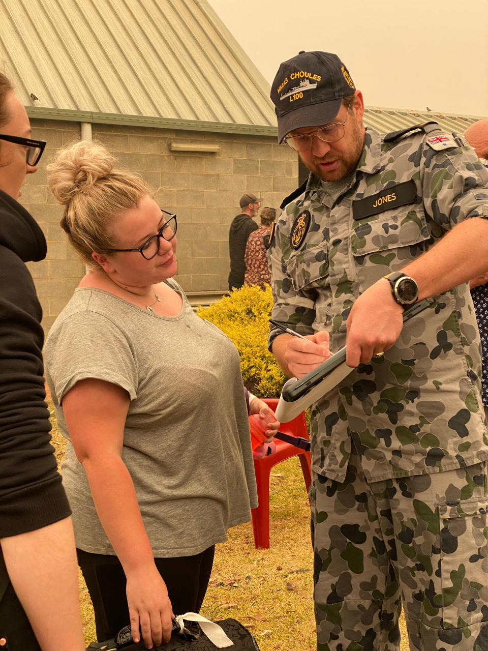 In this photo released and taken Jan. 2, 2020, by the Australian Department of Defense, Chief Petty Officer Maritime Logistics - Personnel Heath Jones checks names of evacuees at the registration point, in Mallacoota, Victoria Australia. Navy ships plucked hundreds of people from beaches and tens of thousands were urged to flee before hot weather and strong winds in the forecast worsen Australia's already-devastating wildfires. (Australian Department of Defense via AP)