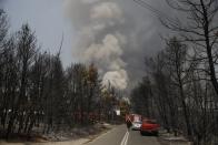 Police and fire block a road as smoke billows from a forest fire in Varibobi area, northern Athens, Thursday, Aug. 5, 2021. Forest fires fueled by a protracted heat wave in Greece raged into Thursday, forcing the evacuation of dozens of villages as firefighters managed to prevent the flames from reaching the archaeological site at the birthplace of the ancient Olympics. (AP Photo/Lefteris Pitarakis)