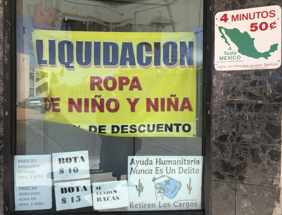 A sign advertising liquidation sales for children's clothes is seen in a window display on March 15, 2021 in downtown Nogales, Ariz. Small businesses in border towns across the U.S. are reeling from the economic fallout of the partial closure of North America's international boundaries. Residents, small business owners and local chambers of commerce say the financial toll has been steep, as have the disruptions to life in communities where it's common to shop, work and sleep in two different countries. A sign posted in the bottom reads in Spanish: "Humanitarian Help is never a Crime. Remove the Criminal Complains." (AP Photo/Suman Naishadham)