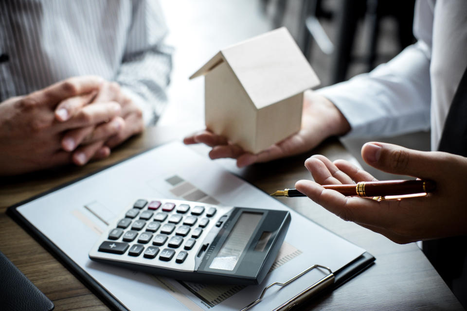 A man discussing Singapore property tax to another person holding a model house with calculator on the table.