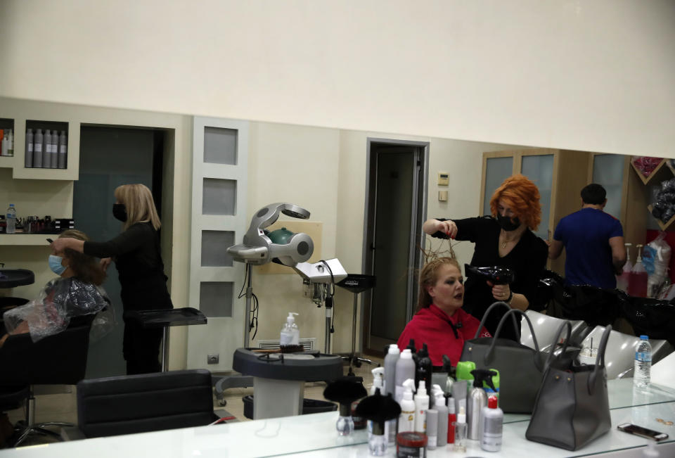 Employees at a hair salon wearing face masks to prevent the spread of coronavirus, work on customers in Athens, Monday, March 22, 2021. Greece's government reopened a limited number of barbershops and hair salons on Monday. (AP Photo/Thanassis Stavrakis)