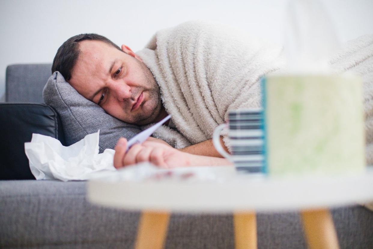 sick man in bed checking fever with thermometer