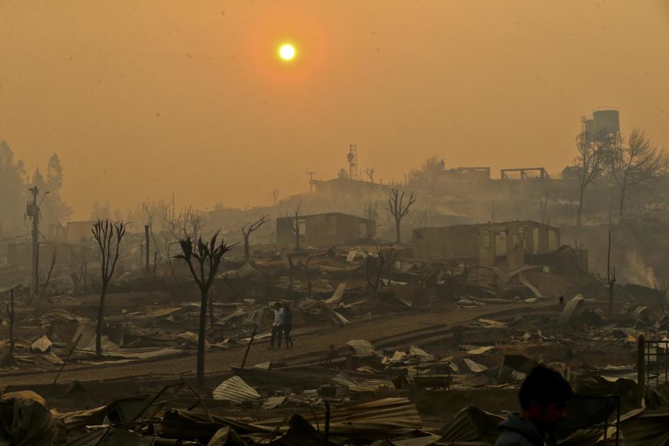 In this Thursday, Jan. 26, 2017 photo, a couple walks through a neighborhood destroyed by wildfires in Chile's Santa Olga community. Officials say the town was consumed by the country's worst wildfires, engulfing the post office, a kindergarten and hundreds of homes. (AP Photo/Esteban Felix)