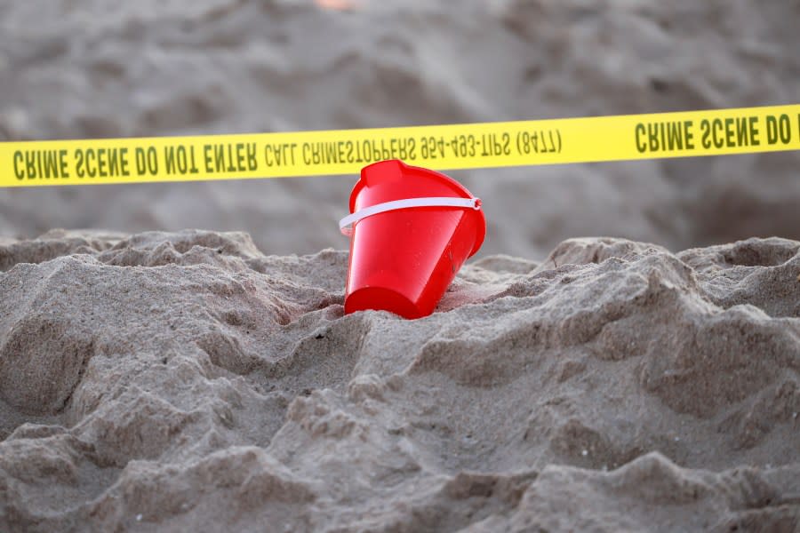 A pail rests next to caution tape on a beach in Lauderdale-by-the-Sea, Fla., on Tuesday, Feb. 20, 2024. A young girl was buried in sand and died Tuesday when a deep hole she was digging with a little boy collapsed on them both at a south Florida beach, authorities said. (Mike Stocker/South Florida Sun-Sentinel via AP)