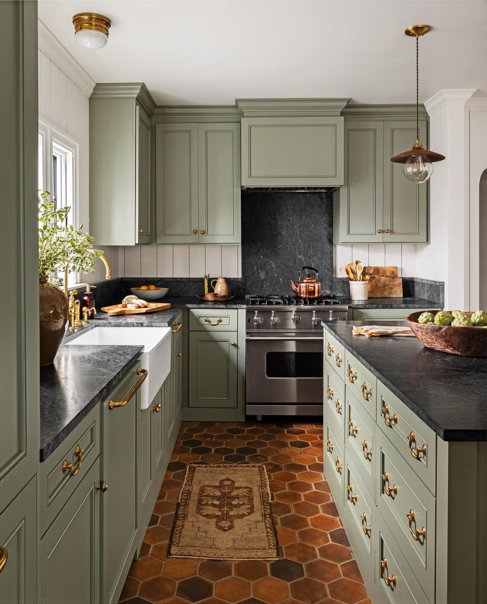 green kitchen cabinets with a warm terra cotta tile floor and black countertops