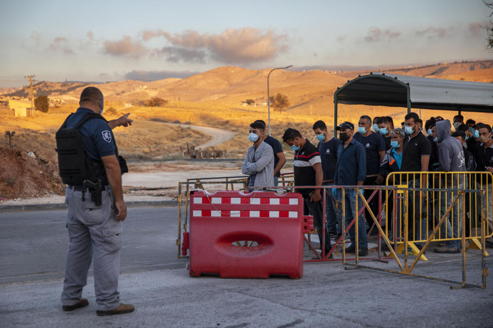 FILE - In this Tuesday, June 30, 2020, file photo,Palestinian laborers line up to cross a checkpoint at the entrance to the Israeli settlement of Maale Adumim, near Jerusalem. Israel's premier human rights group has begun describing both Israel and its control of the Palestinian territories as a single "apartheid" regime, using an explosive term that the Israeli government and its supporters vehemently reject. (AP Photo/Oded Balilty, File)